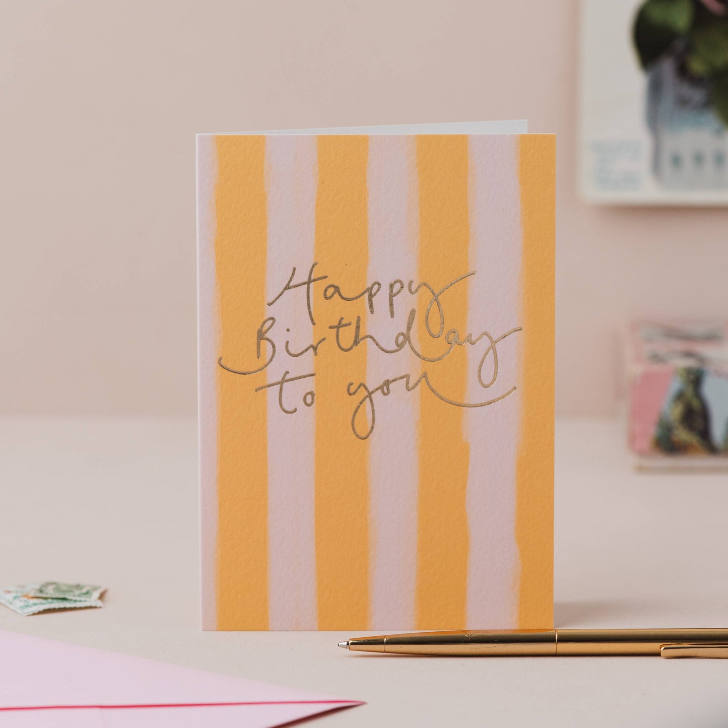 Yellow and white vertically striped greeting card with elegant gold foil cursive lettering reading "Happy Birthday to you".