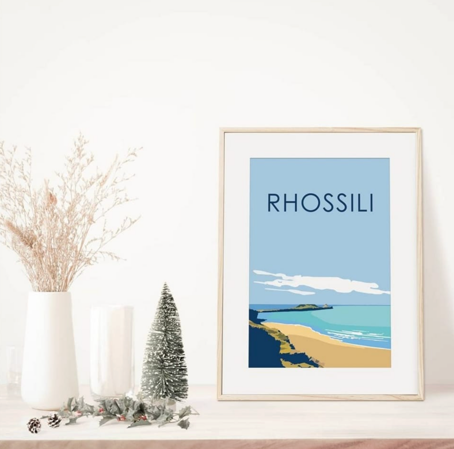 Rhossili Print framed wall art showing Worms Head in pastel tones. Print on shelf with Christmas tree.