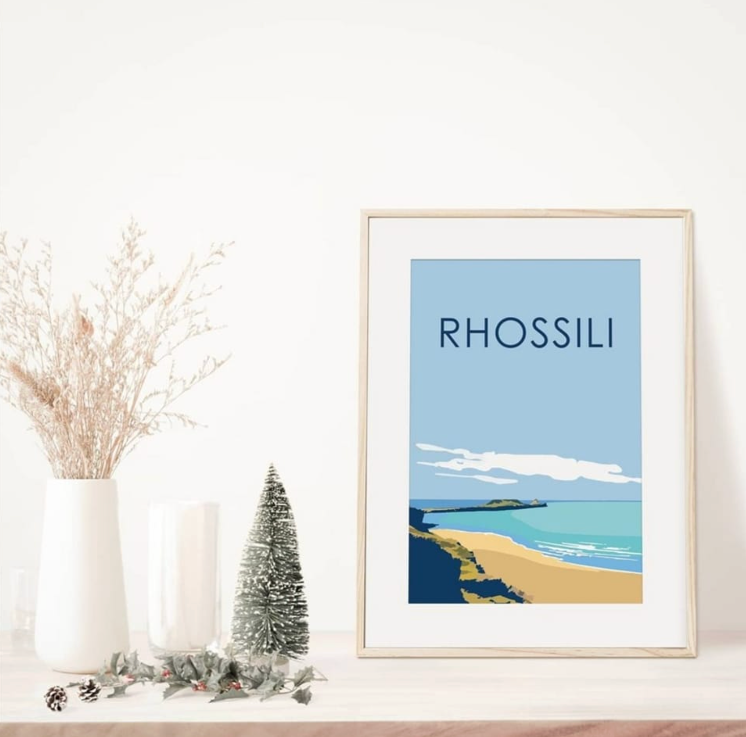 Rhossili Print framed wall art showing Worms Head in pastel tones. Print on shelf with Christmas tree.