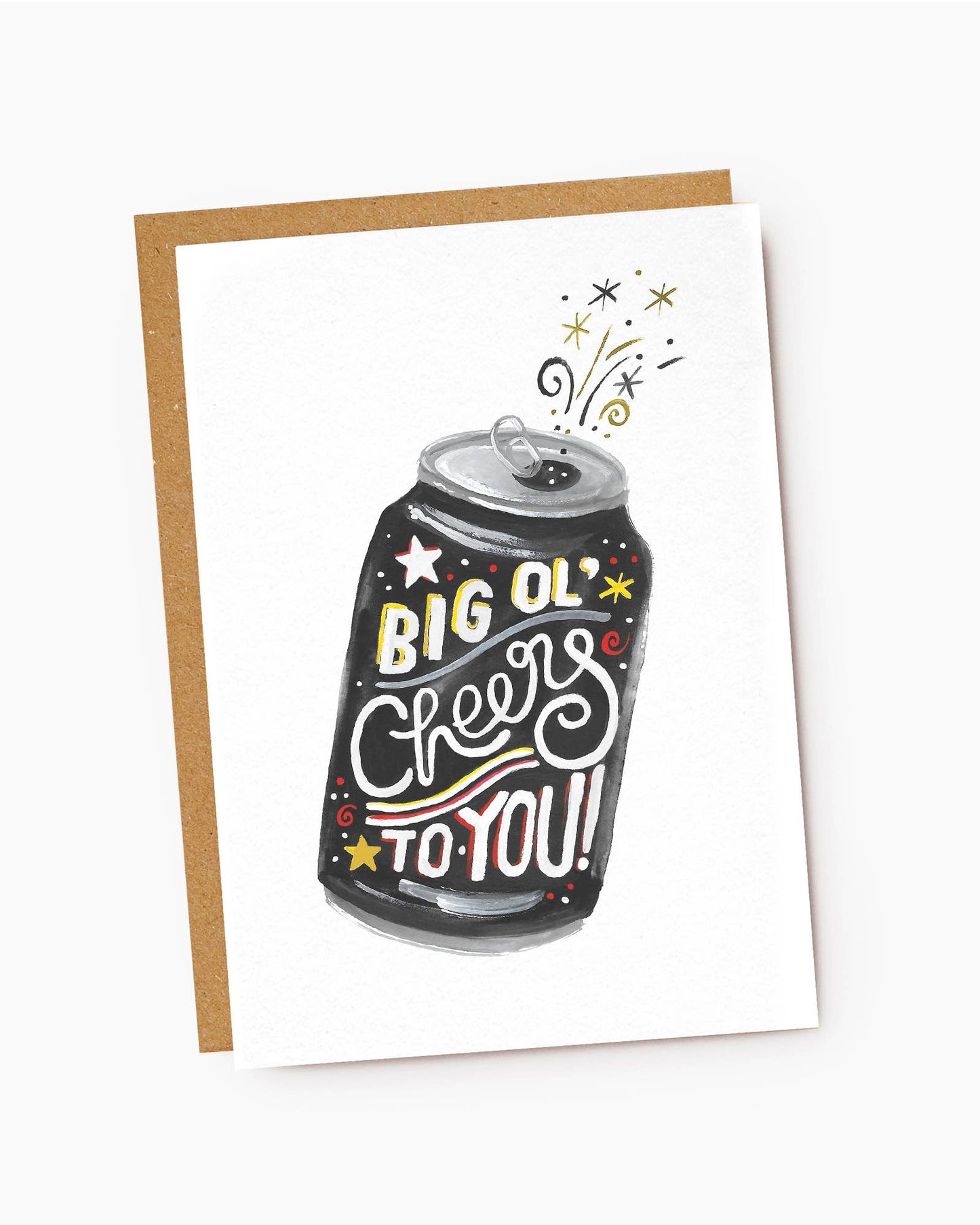 A white textured greeting card featuring a hand-drawn illustration of a dark grey drink can that has just been opened. The front of the can has stylized text that reads "BIG OL' Cheers TO YOU!" in yellow, white, and red lettering, accented by small stars. Whimsical sparkles, swirls, and stars erupt from the open tab at the top, resting on a brown kraft envelope.