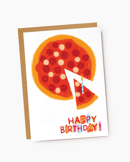A white textured greeting card featuring a playful hand-drawn illustration of a pepperoni pizza with a single slice pulled away. A blue and white striped birthday candle with a lit flame sits on the separated slice. Colorful block lettering at the bottom reads "HAPPY BIRTHDAY!", resting on a brown kraft envelope.