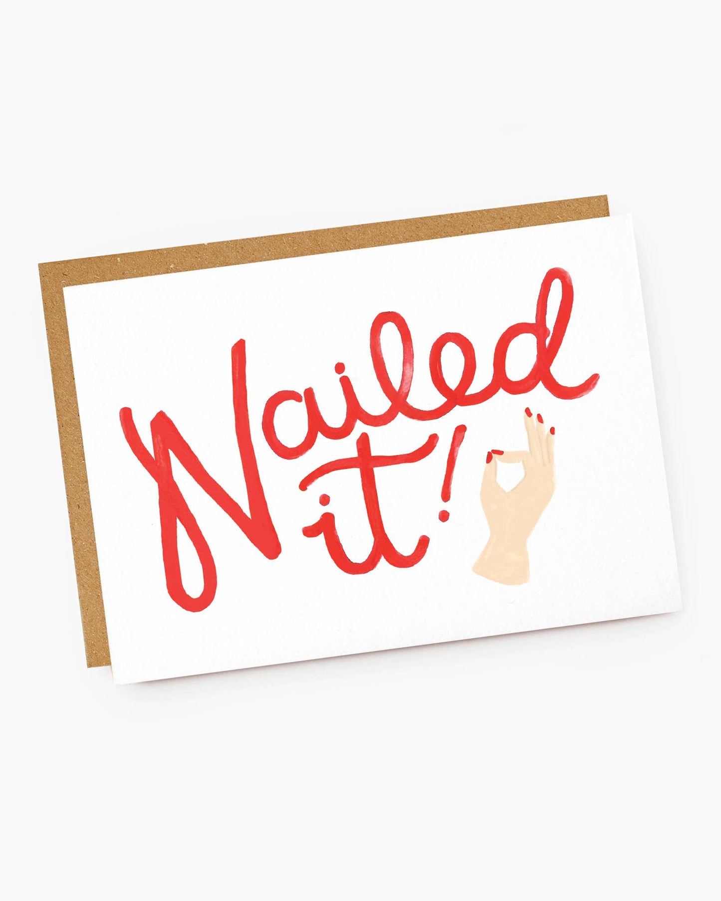 A white landscape-oriented textured greeting card featuring large, expressive red handwritten script that reads "Nailed it!". To the right of the text, a small hand illustration with bright red painted fingernails makes a perfect "OK" gesture, resting on a brown kraft envelope.