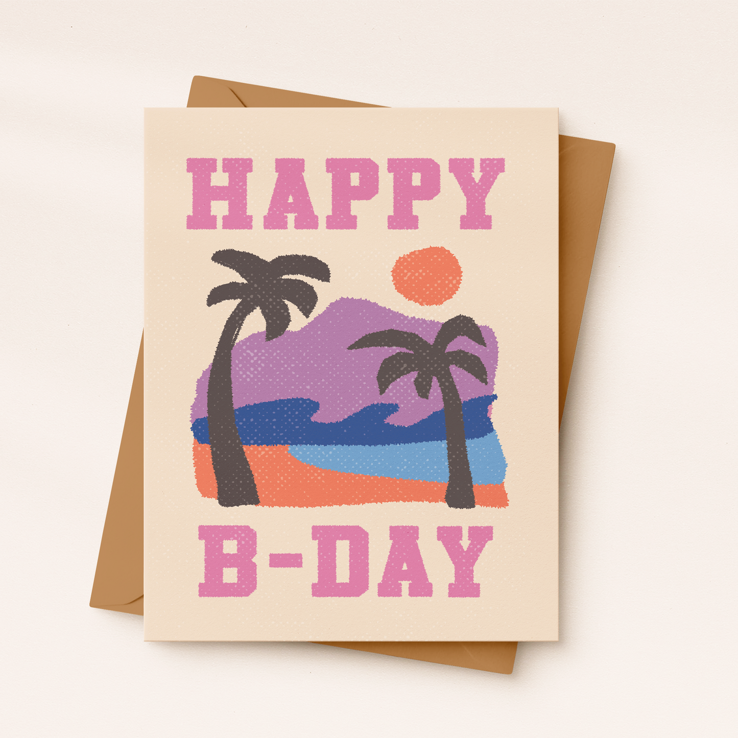 A cream-colored textured greeting card with a retro sunset illustration featuring a purple mountain, deep blue sea waves, two black palm trees, and an orange sun. Bold pink collegiate-style text reads "HAPPY" at the top and "B-DAY" at the bottom, resting on a brown kraft envelope.