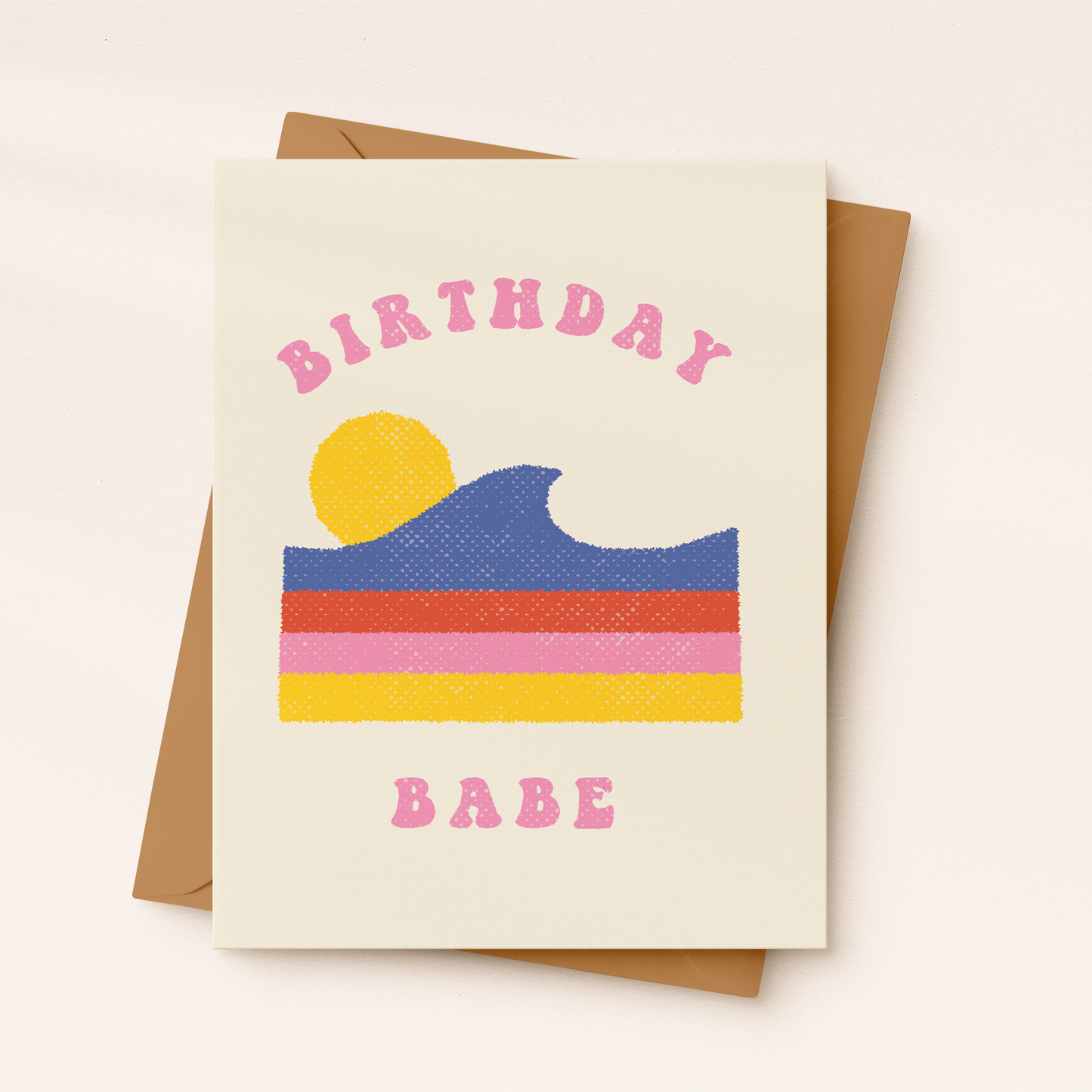 A cream-colored textured greeting card featuring a retro-style graphic of a blue cresting ocean wave layered over horizontal red, pink, and yellow stripes, with a yellow sun in the background. Pink curved block text reads "BIRTHDAY" at the top and "BABE" at the bottom, resting on a brown kraft envelope.